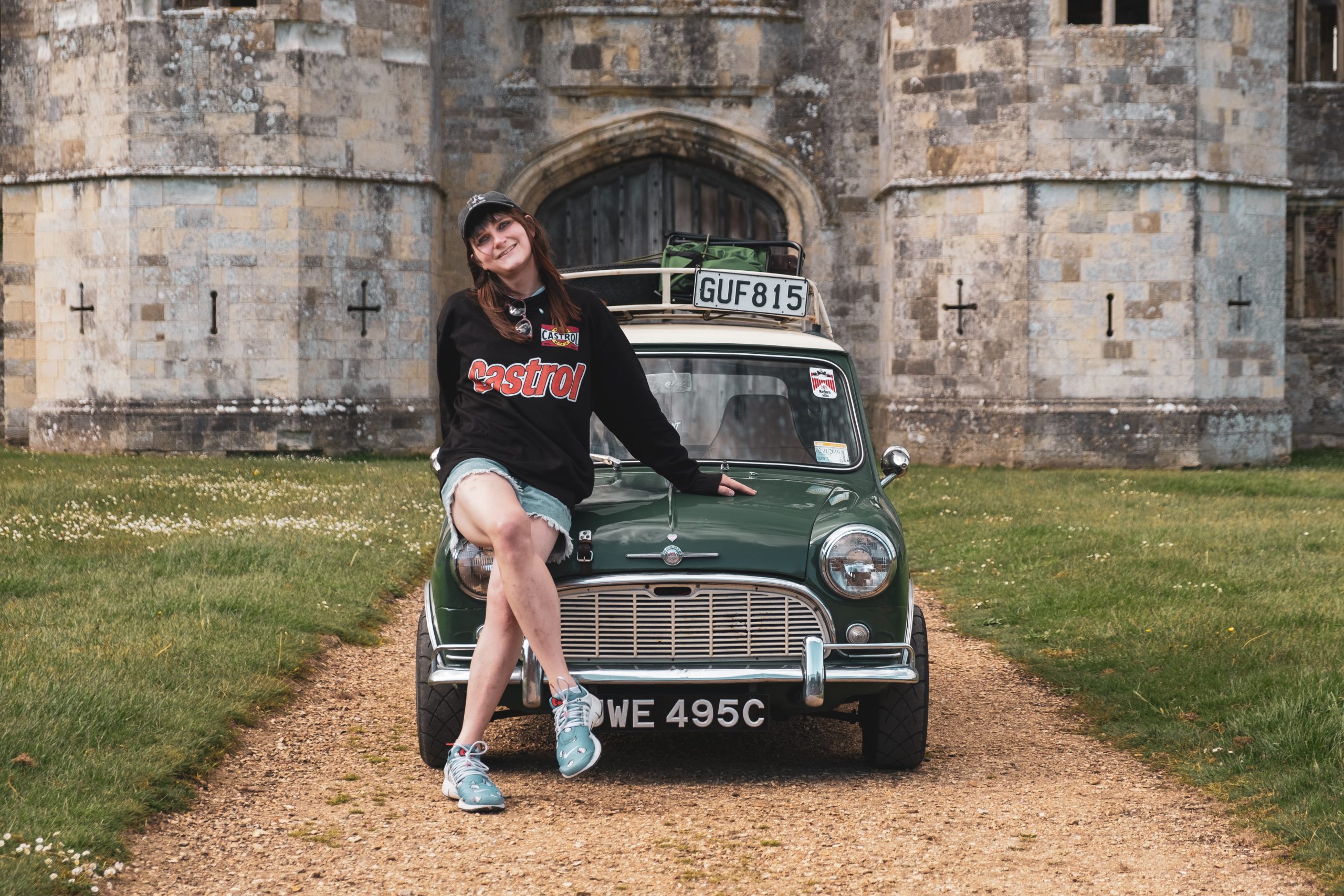 A woman in casual clothing, sitting on the front of a green classic Mini car